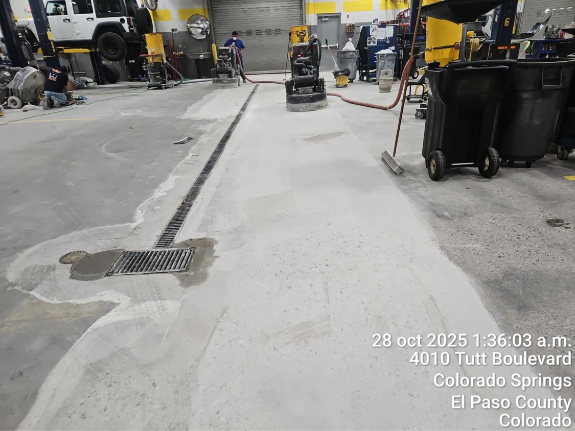 Ground section of auto shop floor in Colorado Springs showing the opened slab beside unground concrete, with grinders working in the background
