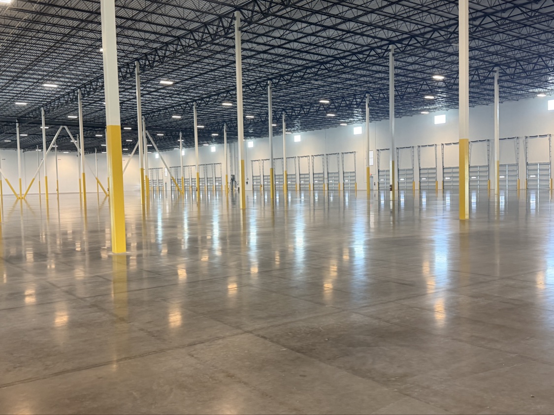 Mirror-polished concrete floor reflecting columns and dock doors across a huge finished distribution center