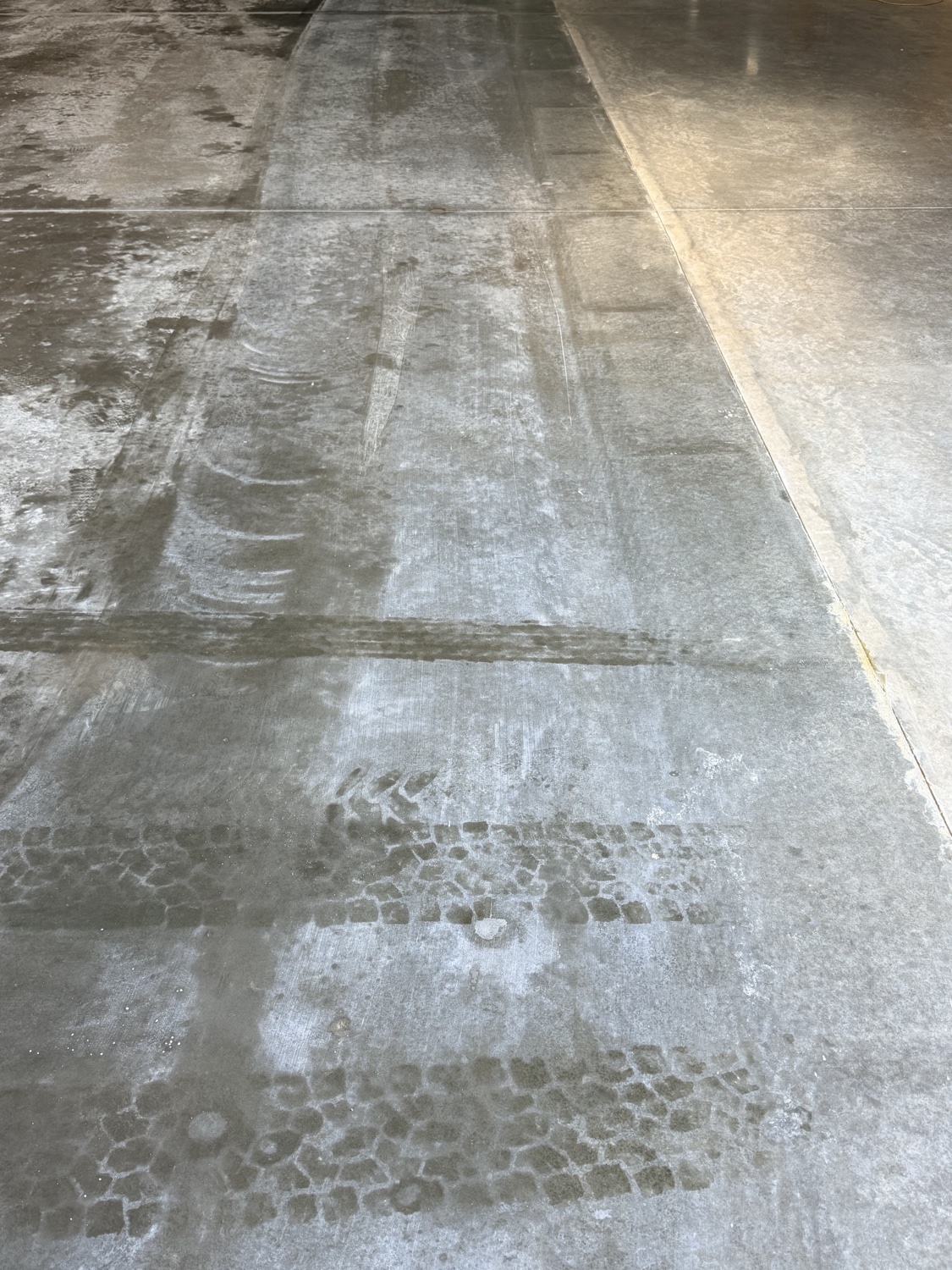 Close-up of a sweating slab — moisture sheen on the concrete with wet forklift tire tracks through it