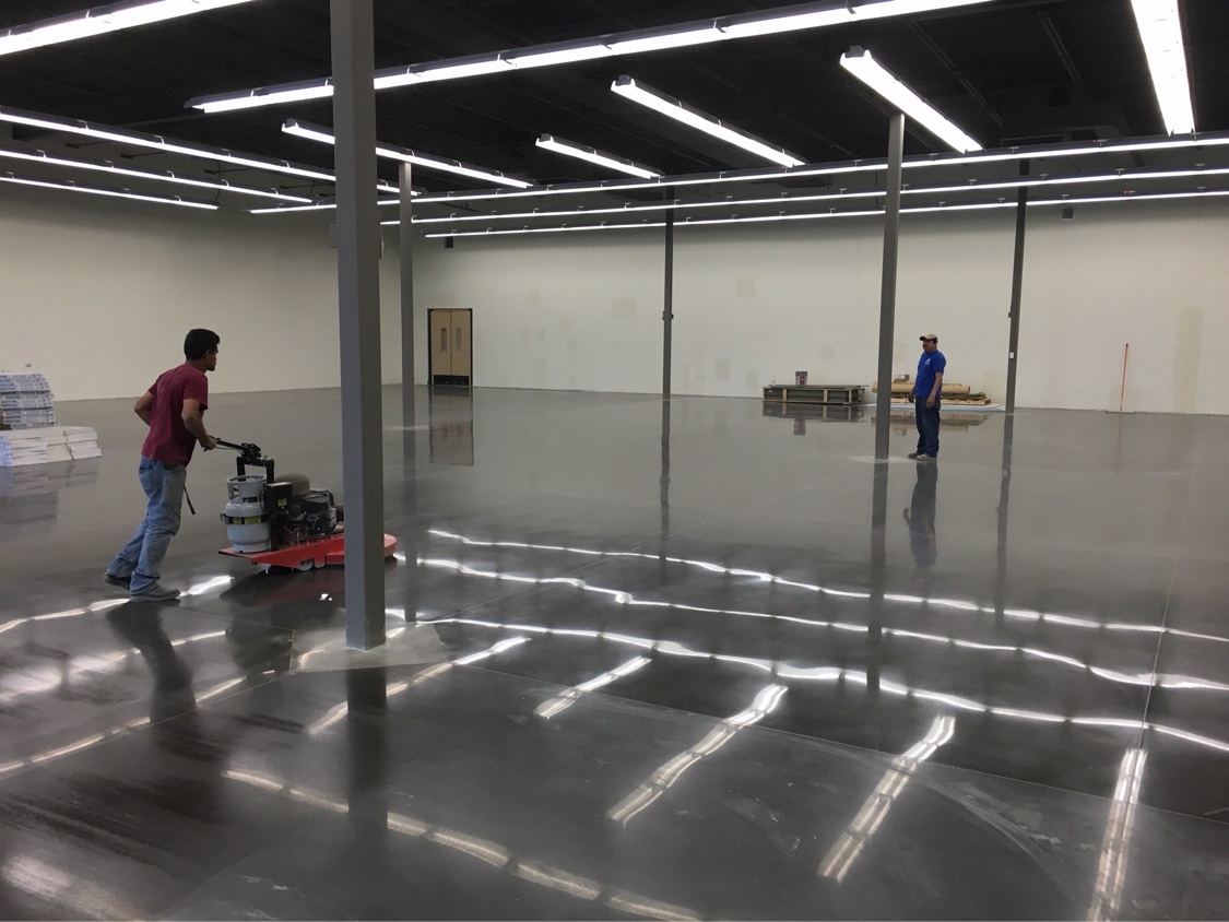 Crew member running a burnisher across a dark mirror-stained concrete floor in an empty retail space