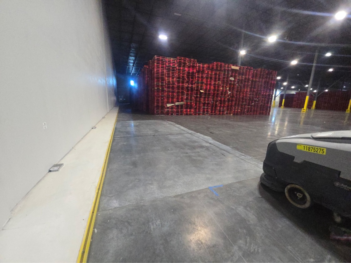 Wide warehouse floor under treatment, flanked by tall stacks of red pallets