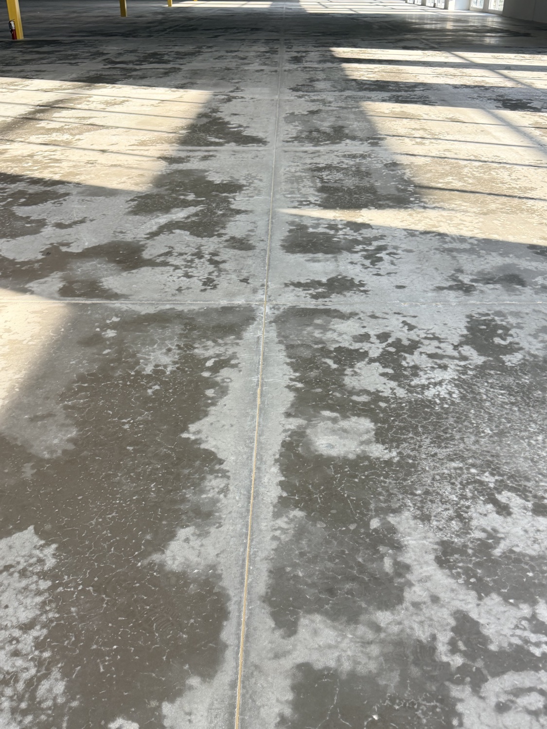 Mottled moisture pattern spreading across a sweating warehouse slab